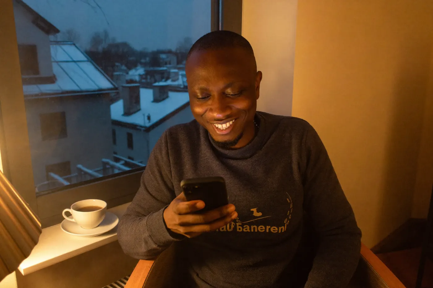 Un homme sourit à son téléphone, l'hiver derrière la fenêtre.
